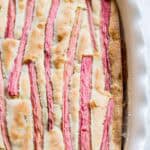 Close-up view of a rhubarb cake in a baking dish showing bright pink rhubarb stalks embedded in golden cake batter.