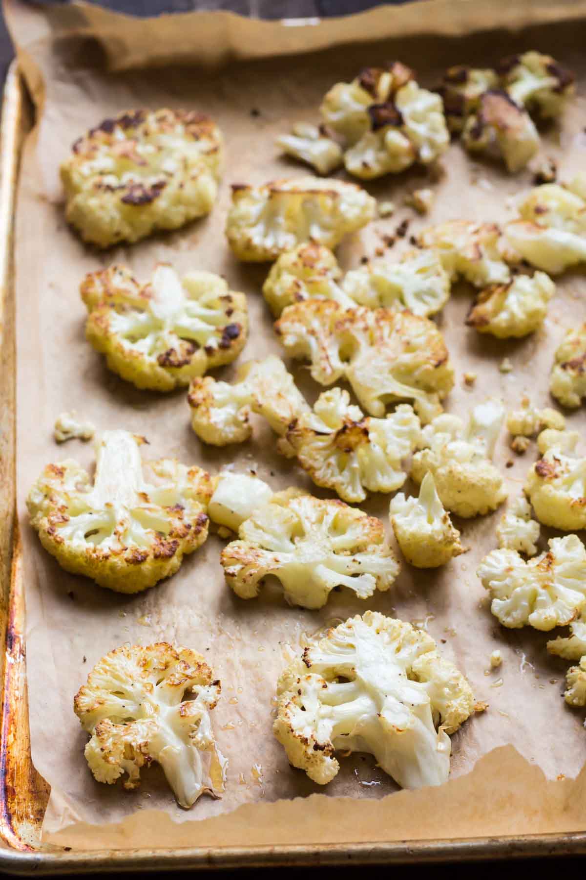 Roasted cauliflower florets with golden-brown edges arranged on a baking sheet lined with parchment paper.