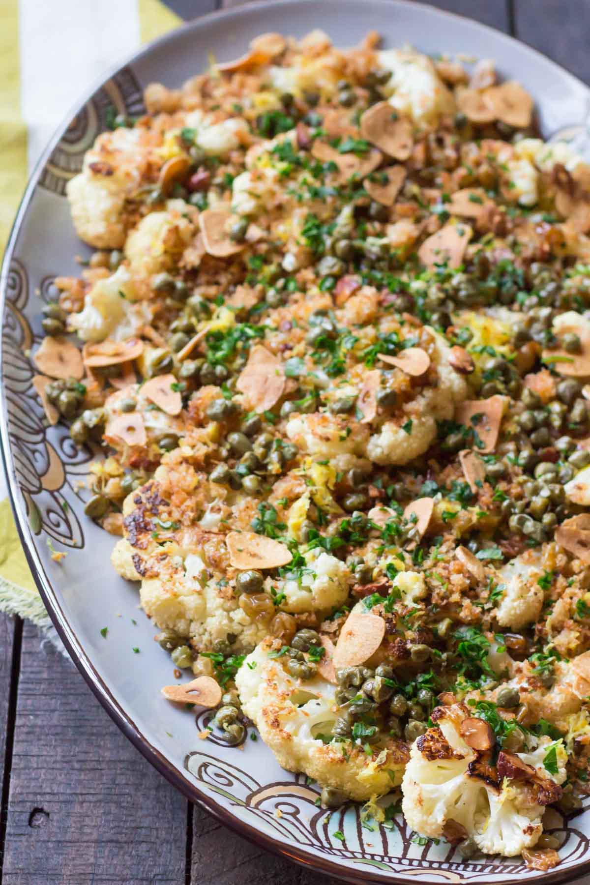 A decorative serving platter filled with roasted cauliflower topped with a flavorful mixture of breadcrumbs, capers, fresh herbs, and sliced almonds.