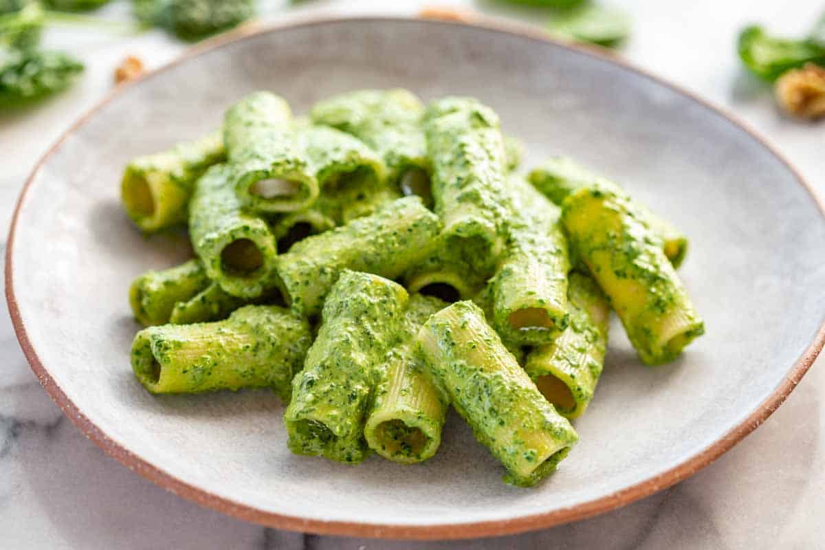 Close-up of rigatoni pasta tossed in bright green spinach pesto, showing the texture of the sauce clinging to the ridged pasta tubes.