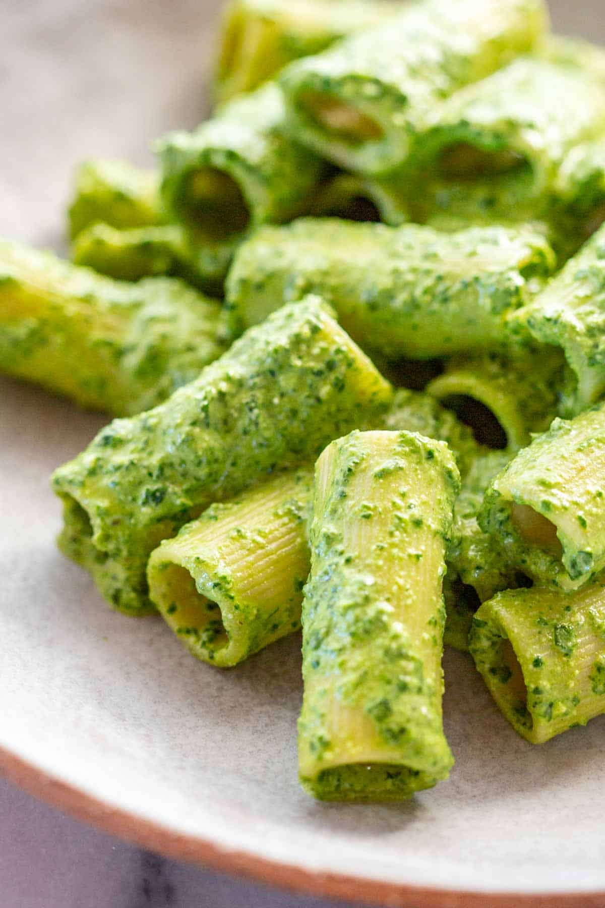 Macro shot of rigatoni pasta pieces covered in bright green pesto sauce, showing the texture and thickness of the sauce on the pasta.