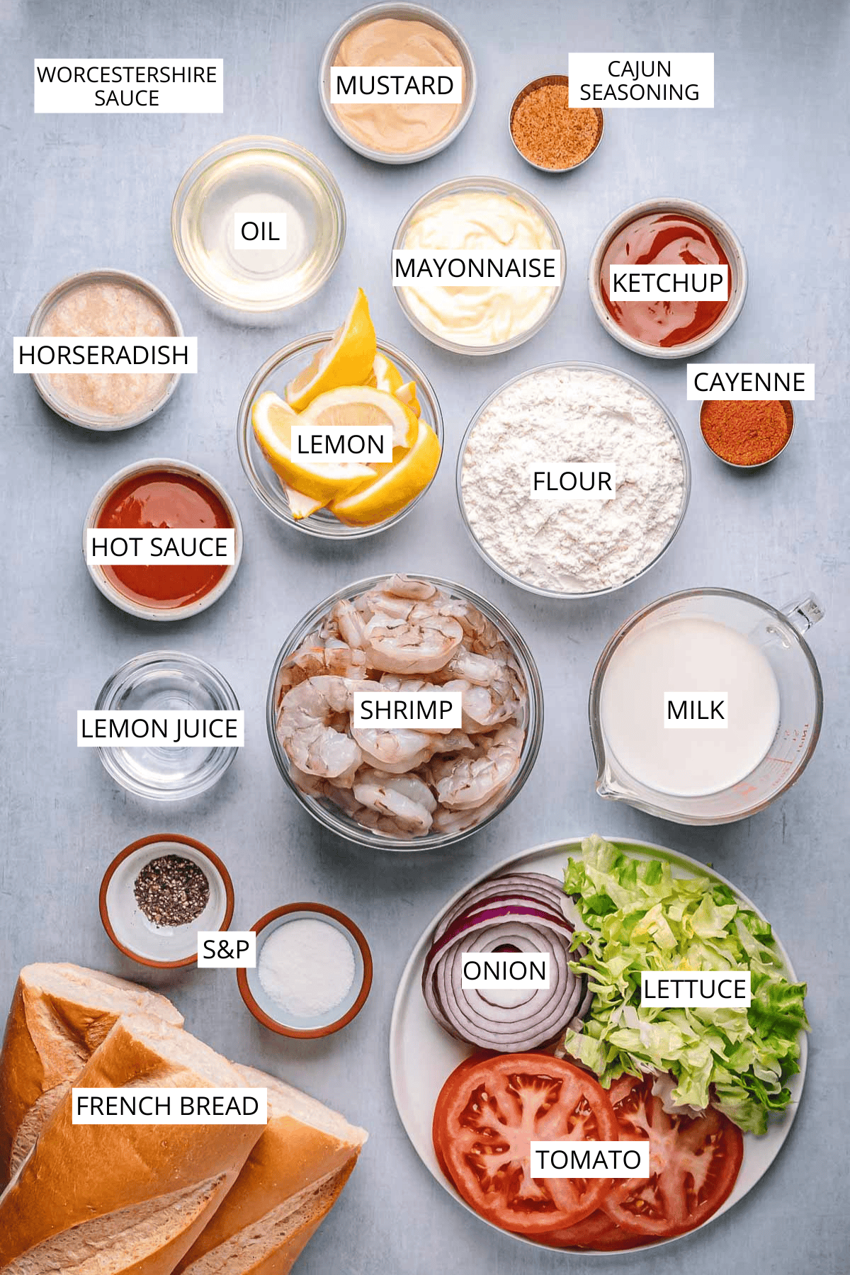 Flat lay of labeled ingredients for a shrimp po'boy, including raw shrimp, French bread, lettuce, tomato, red onion, milk, flour, and condiments like mayonnaise, ketchup, mustard, hot sauce, and seasonings.