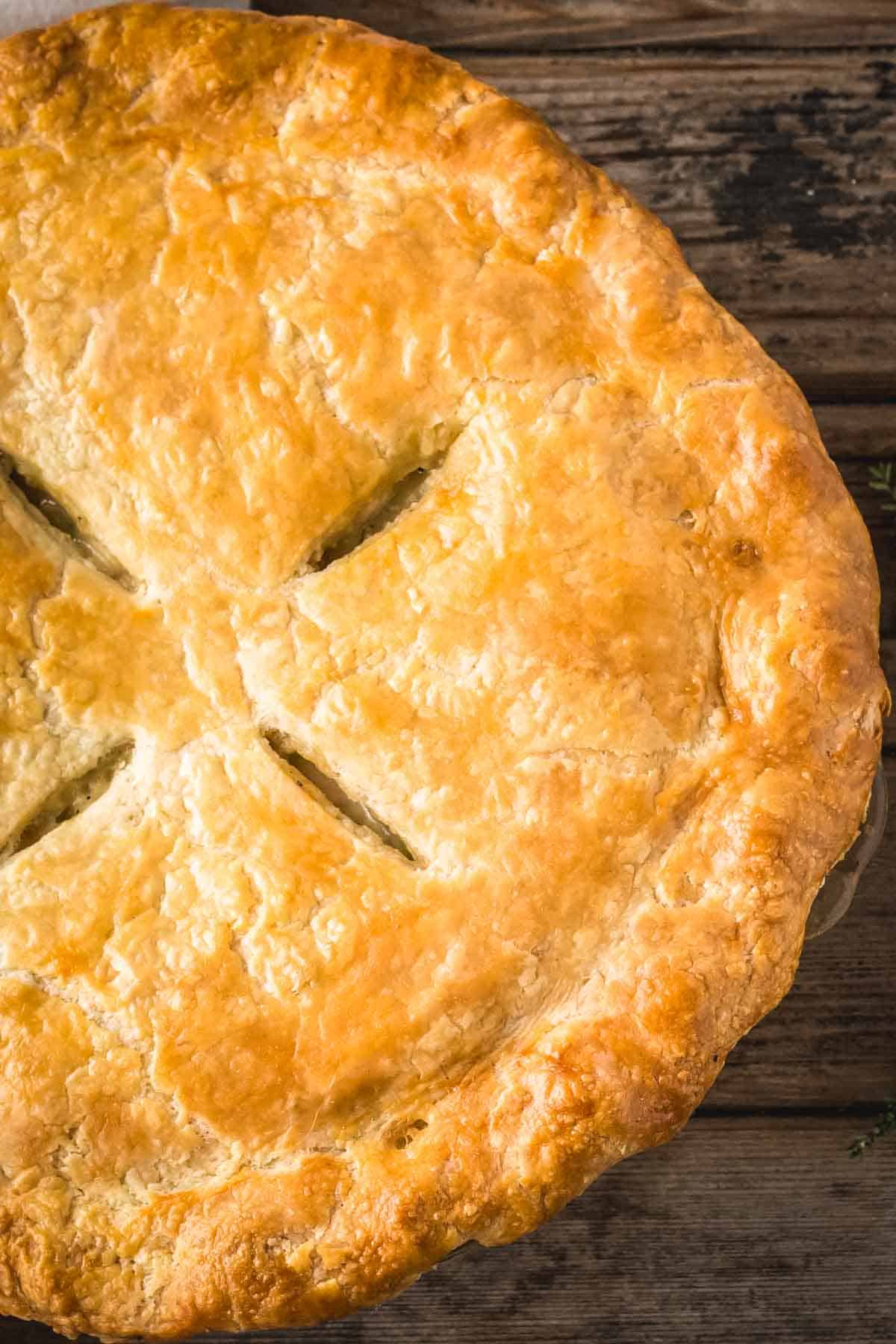 Overhead shot of the whole chicken pot pie with its golden homemade crust and four slithers used to take out the moisture during baking.