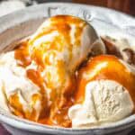Close-up of scoops of vanilla ice cream in a rustic ceramic bowl, generously drizzled with a thick, golden homemade salted caramel sauce.