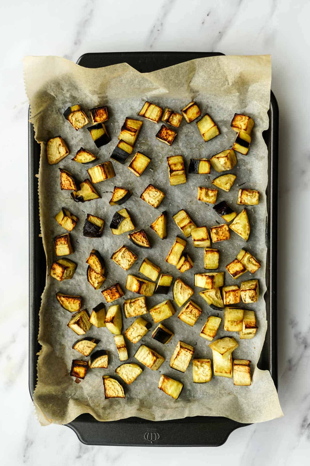 Roasted eggplant cubes on a parchment-lined baking tray. Unlike Image 1, these pieces are now golden brown with caramelized edges, showing they've been roasted to develop deeper flavor for the pasta dish.