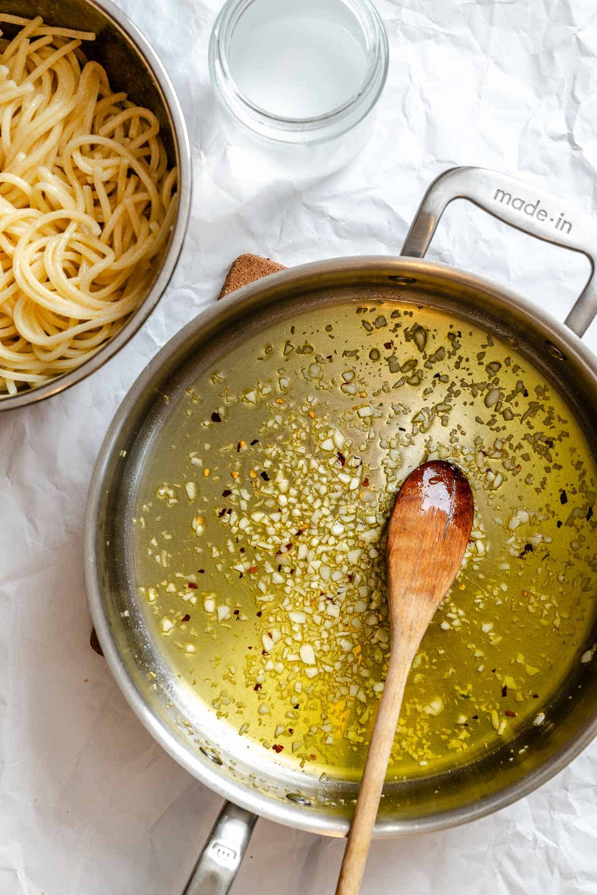A cooking setup featuring a pot of cooked spaghetti on the left and the garlic-infused olive oil sauce in a saucepan on the right. This image captures the moment before combining the pasta with the flavored oil, showing both key components ready to be united.