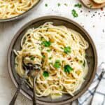 The finished pasta aglio e olio served in a rustic ceramic bowl and garnished with fresh parsley. The glossy spaghetti shows traces of the garlic, oil, and red pepper flakes coating each strand. A pair of serving utensils rest in the dish, ready for serving.