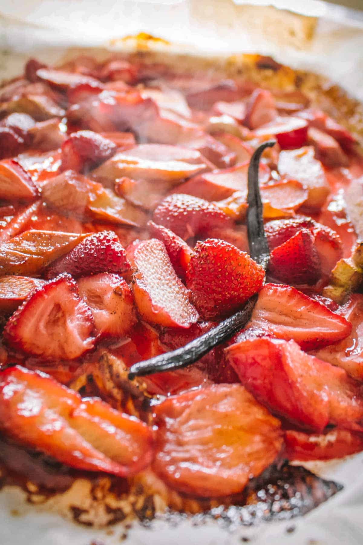 Close-up of a baking dish filled with strawberry-rhubarb filling showing sliced strawberries, rhubarb pieces, and vanilla bean in a glossy, ruby-red syrup. The mixture is ready to be spooned over shortcakes.