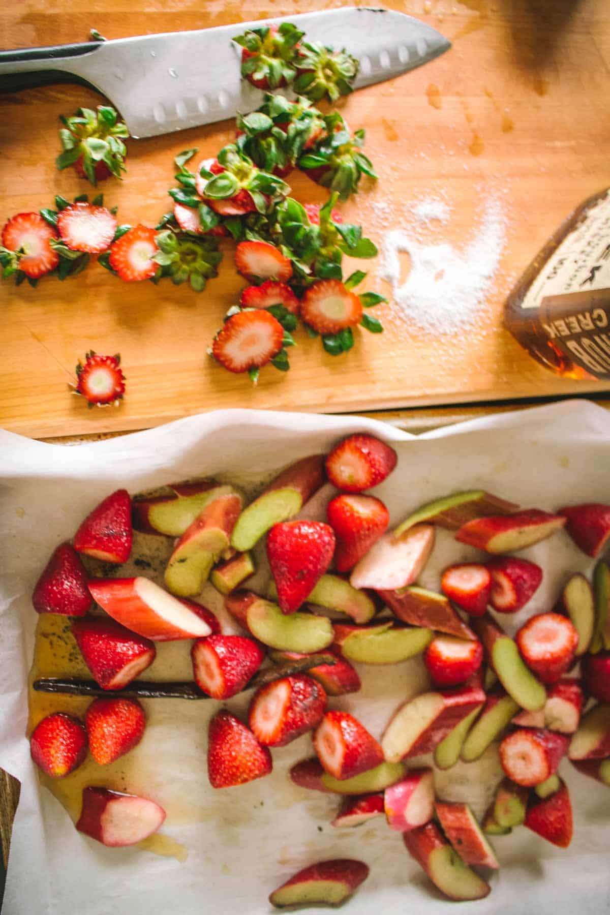 Preparation shot showing sliced strawberries with stems and sliced rhubarb on a wooden cutting board. A chef's knife is visible, capturing the process of preparing fruits for the filling.