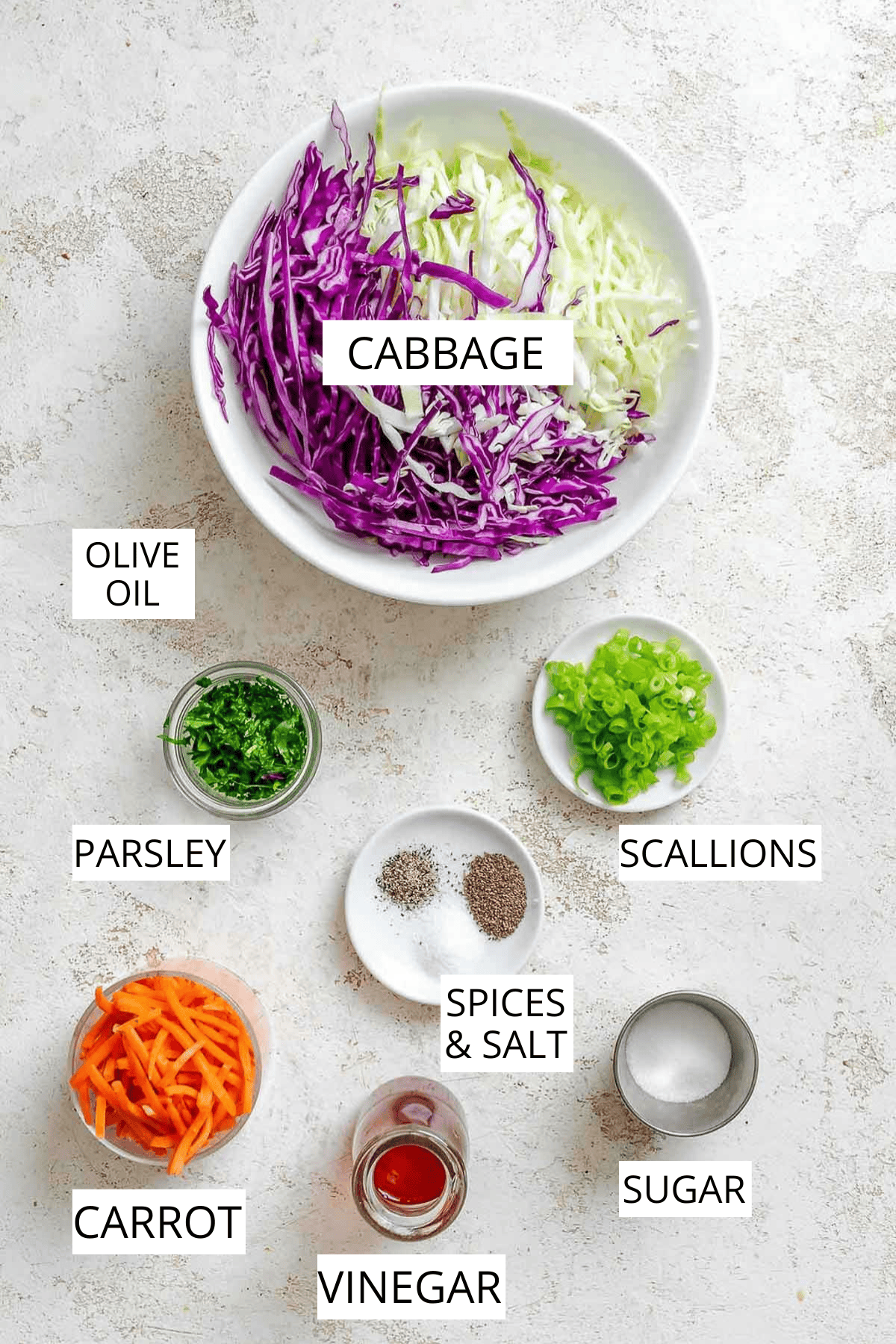 A flat lay of the slaw ingredients, including shredded cabbage, carrots, parsley, green onions, sugar, salt, pepper, and red wine vinegar, arranged neatly on a white countertop.