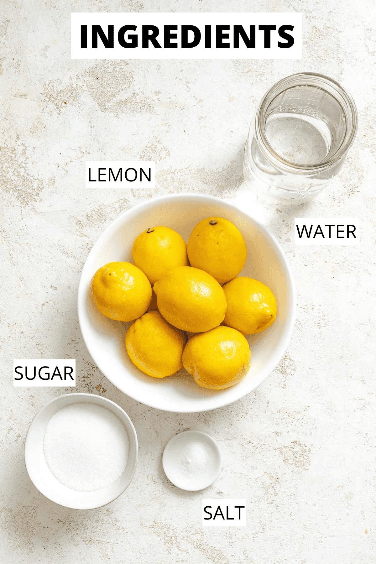 Overhead view of whole lemons, granulated sugar, and salt arranged on a countertop next to a mason jar of water-ingredients staged for making lemon granita.