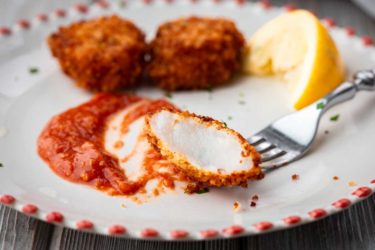Bite of panko scallop held on a fork above cocktail sauce, revealing the juicy interior.