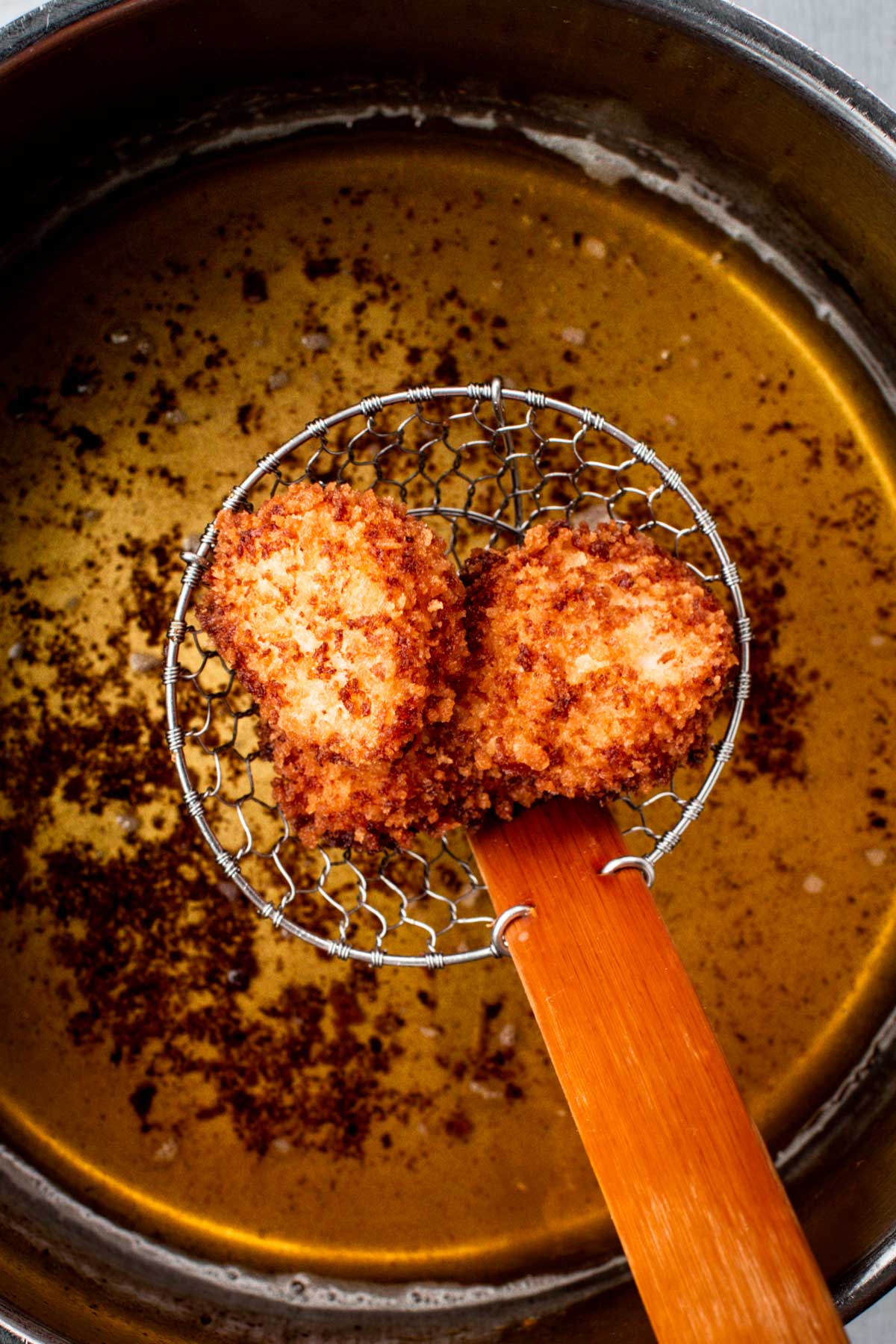Wire skimmer lifting two golden brown panko-crusted scallops over the fryer.