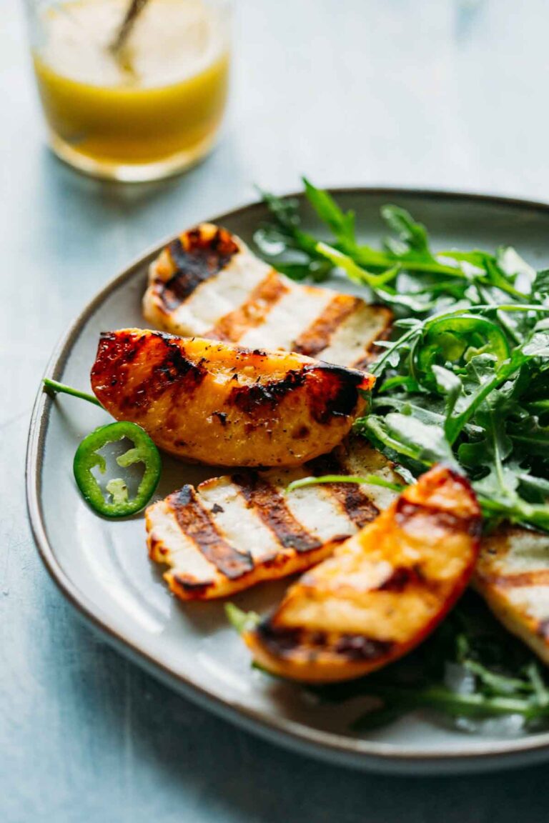 Grilled peaches and halloumi nestled on greens, served with jalapeño and honey vinaigrette in the background.