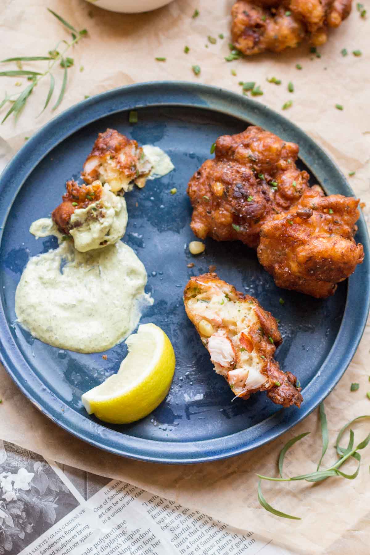 Overhead view of a blue plate with half-eaten fritters, tarragon aioli smeared on the plate, and a lemon wedge.