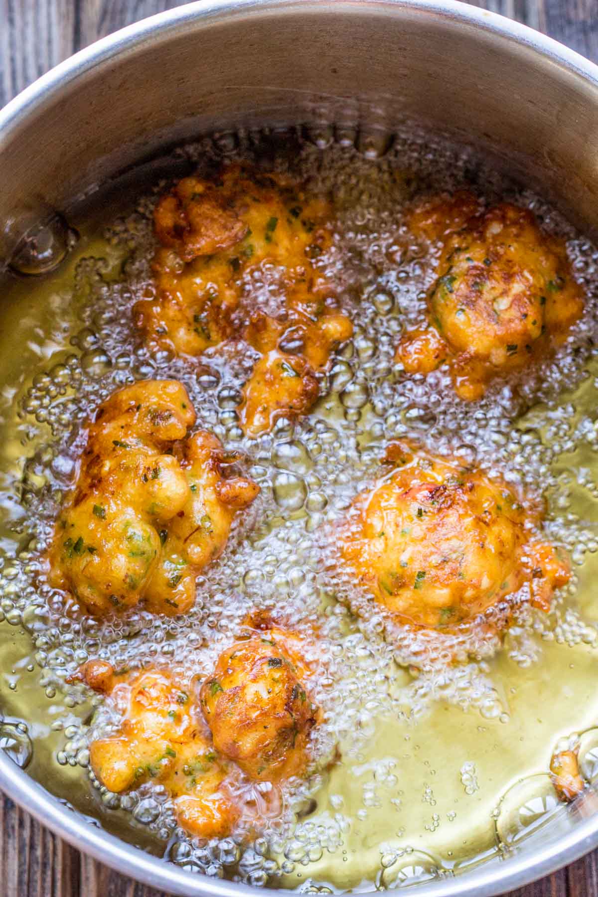Fritters bubbling in hot oil inside a stainless steel pot, turning crisp and golden as they fry.