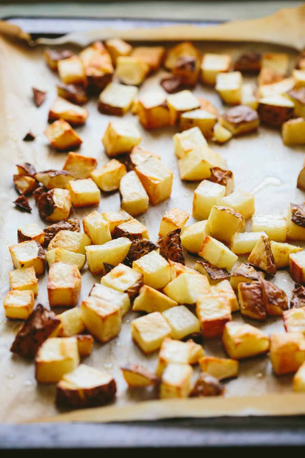 Sheet pan with freshly roasted potato cubes, golden and crisp on the outside, cooling on parchment paper.