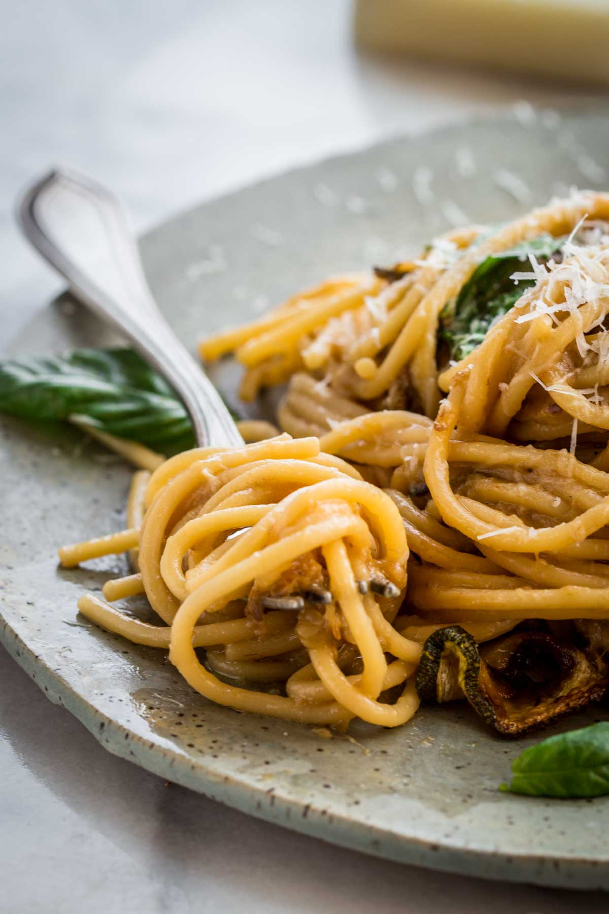 A tight close-up of a forkful of spaghetti alla Nerano being lifted from the edge of the plate, highlighting the creamy coated noodles and bits of caramelized zucchini clinging to the strands.