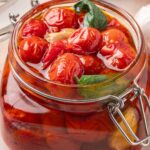 Zoomed-in view of cherry tomato confit packed in a glass jar with basil and oil.