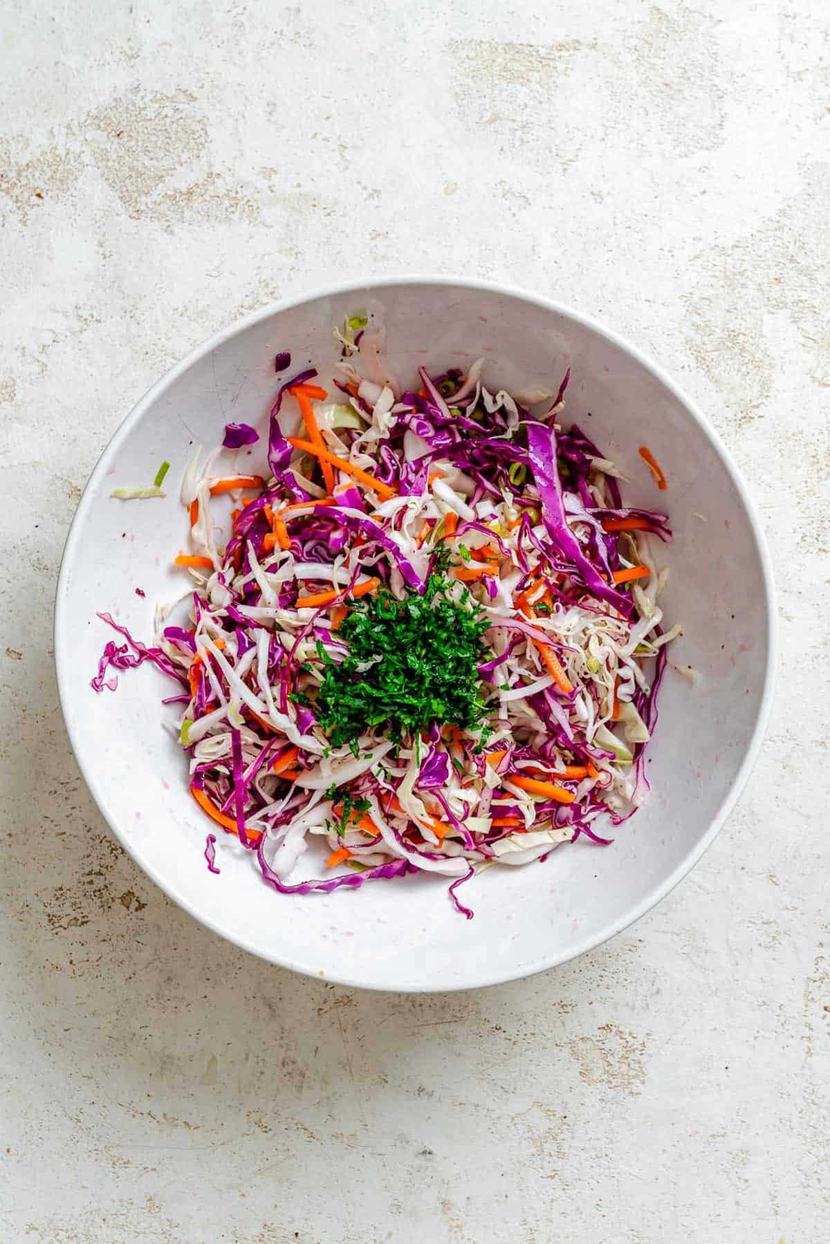 A bowl of mixed vinegar slaw topped with a fresh mound of finely chopped parsley, ready to be tossed.