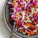 The colorful slaw mixture is shown in detail with a fork resting inside the bowl, emphasizing the crunchy vegetables and herbs.