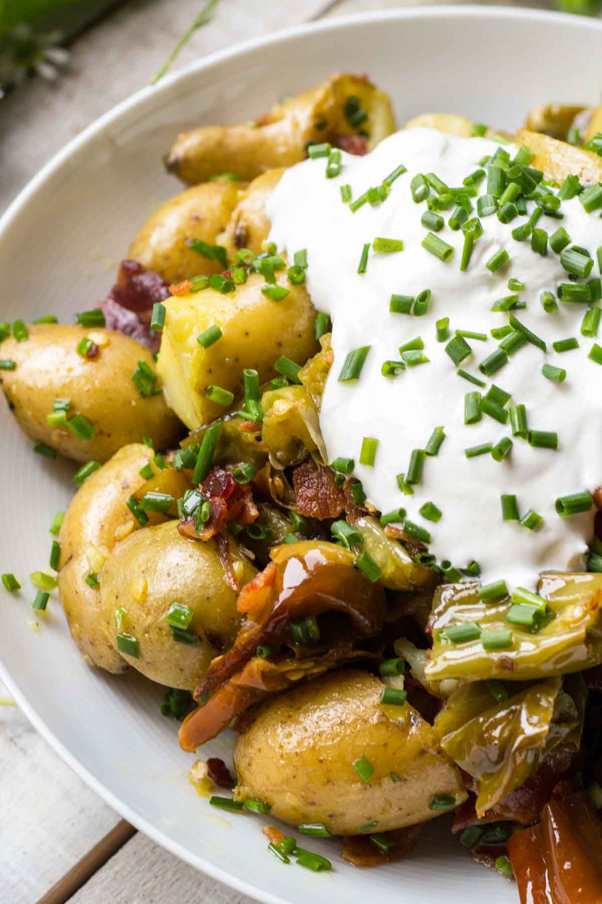 Side view of the potato salad showing chunks of roasted long hot peppers, golden potatoes, and bacon under a mound of sour cream and chives.