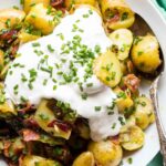 Bright, top-down shot of the plated salad with a large spoon, displaying the textures of the potatoes, herbs, and toppings.