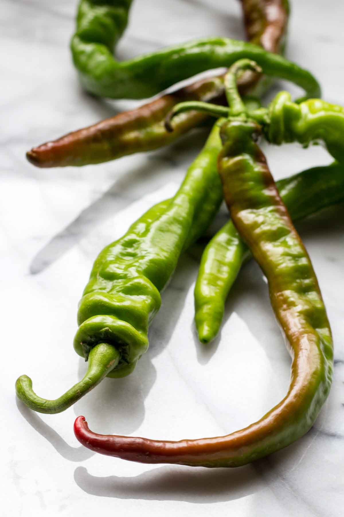 A few whole long hot peppers resting on a marble surface, some with deep red tinges, emphasizing their fresh, wrinkled skins and curvy stems.