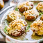 Sharp foreground focus on cheesy, breadcrumb-topped baked tomatoes with melted cheese edges and flecks of green herbs.