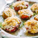 Zoomed-in shot of baked tomatoes covered in bubbly cheese and crispy panko, garnished with thyme on a decorative platter.