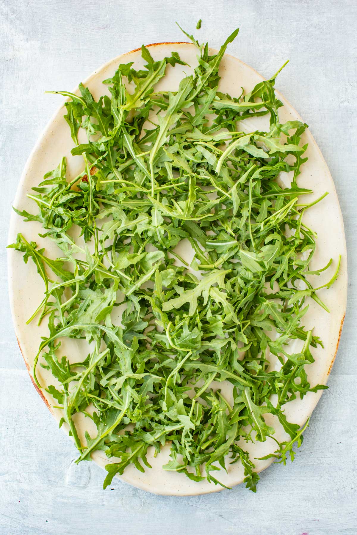 A large oval platter spread with a bed of fresh arugula, ready to be topped.