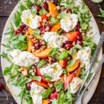 Full top-down view of the finished cherry peach burrata salad on a large platter with serving utensils and scattered ingredients.