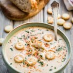 Overhead shot of crab soup garnished with herbs and oyster crackers, with rustic bread slices and a spoon in the background.