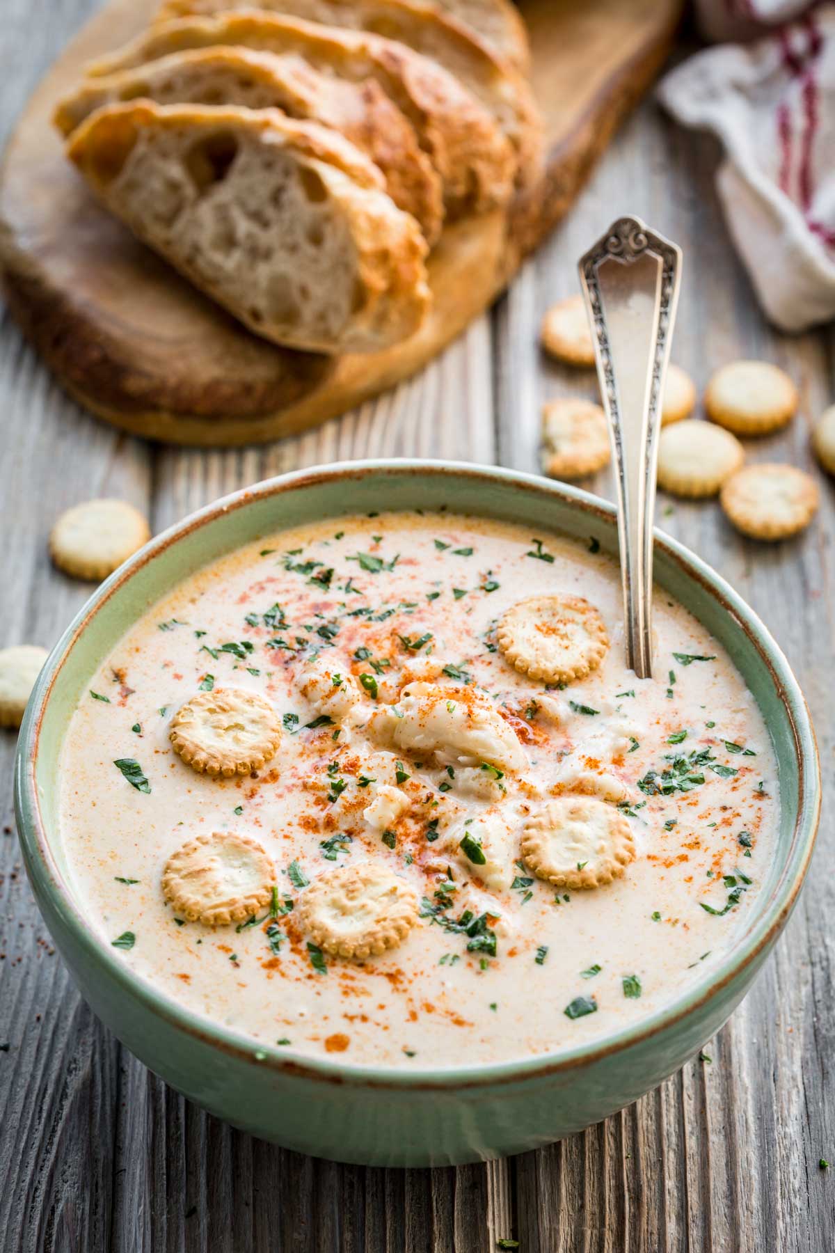 Overhead shot of crab soup garnished with herbs and oyster crackers, with rustic bread slices and a spoon in the background.