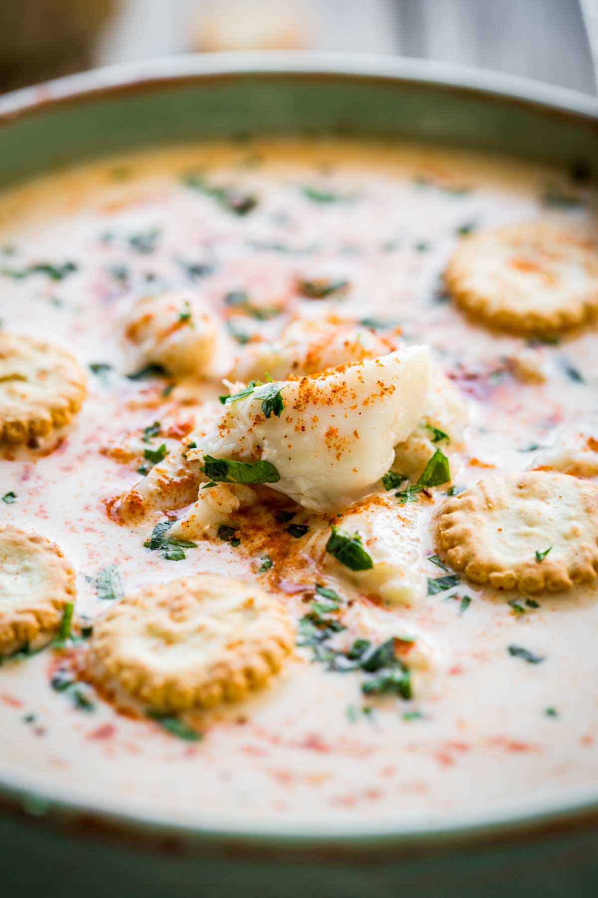 Detail shot of a large chunk of lump crab meat in creamy soup, surrounded by herbs and crackers.