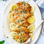 Breaded flounder francaise arranged over lemon slices on a white serving dish, topped with lemony butter sauce and fresh parsley.