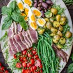 Colorful fresh tuna Niçoise salad styled on a rustic wood background with vibrant ingredients including green beans, potatoes, eggs, and tomatoes.