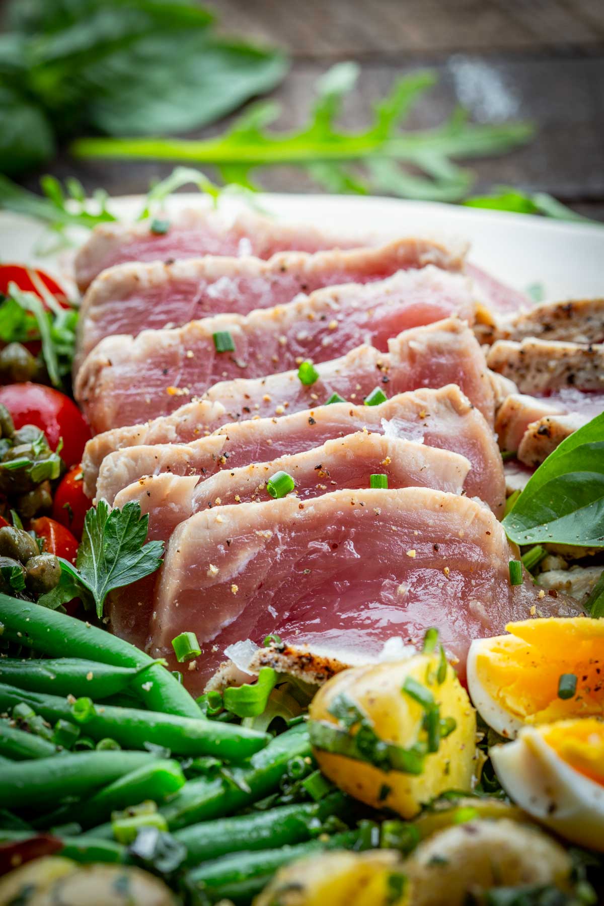 Detail shot of perfectly seared rare tuna slices on arugula, surrounded by green beans, potatoes, and eggs.