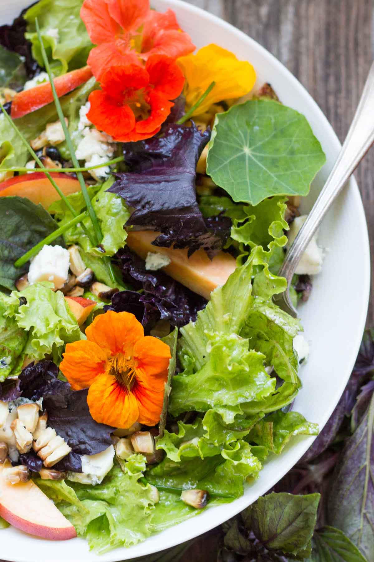 Overhead view of a vibrant salad with leafy greens, nectarines, blue cheese, chopped grilled corn, and orange nasturtium flowers.
