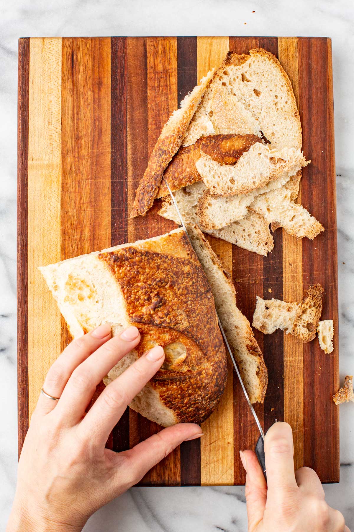 Slicing crusty sourdough bread on a wooden cutting board, with crust being removed.