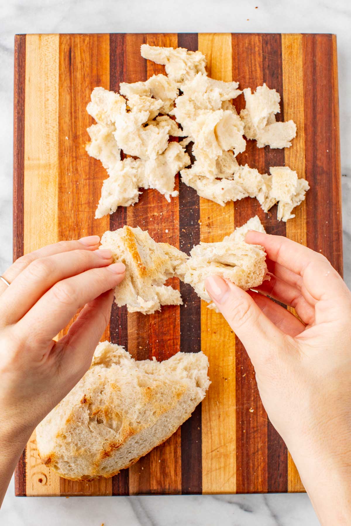 Hands tearing soft bread into bite-sized chunks on a cutting board.
