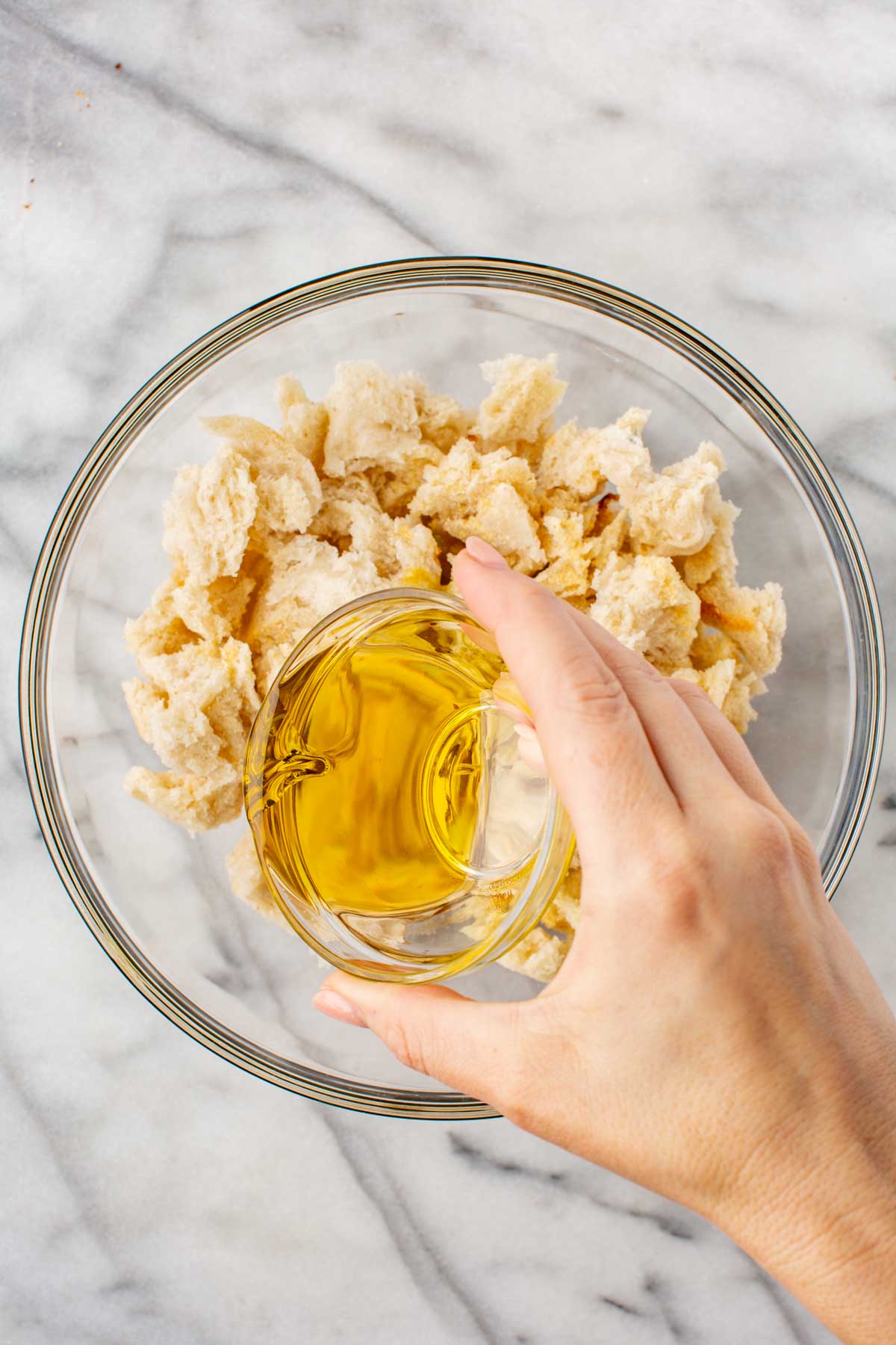 Pouring olive oil over a bowl of torn bread pieces before baking.