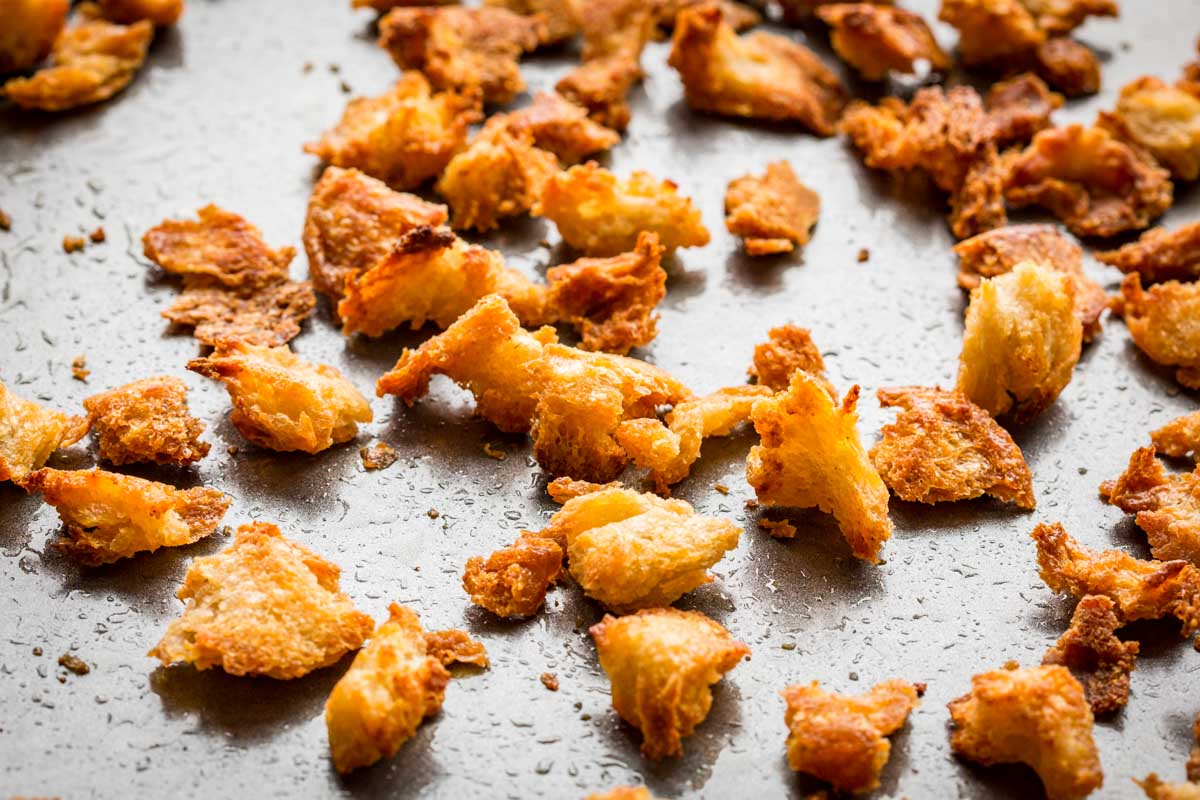 Close-up of crispy homemade croutons scattered on a baking sheet.