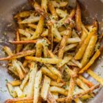Close-up of freshly baked truffle fries in a stainless steel mixing bowl, coated with Parmesan cheese and herbs.