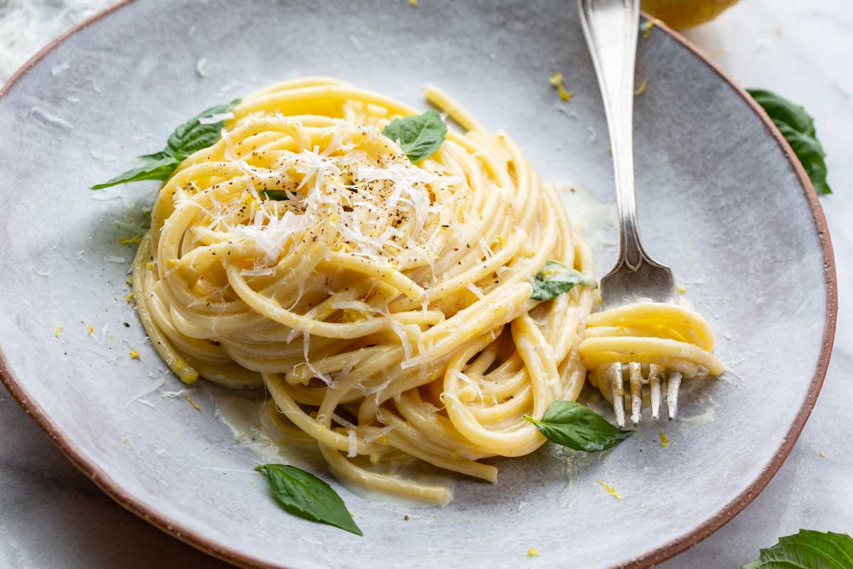Angled view of a finished plate of pasta al limone, showcasing its creamy lemon sauce, fresh basil, and shaved Parmesan with a fork twirl.