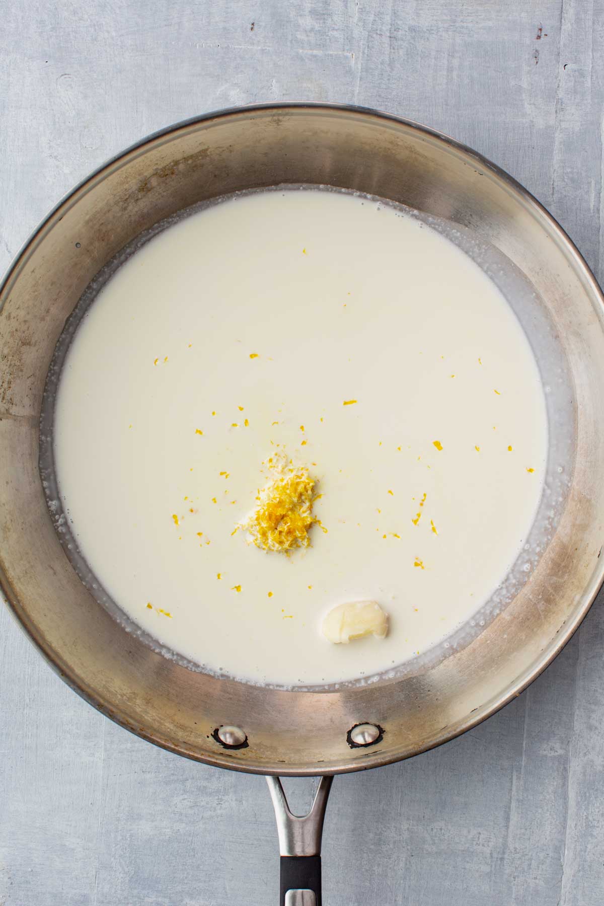 Lemon zest and a clove of garlic in heavy cream inside a stainless steel skillet, the base for creamy pasta al limone sauce.