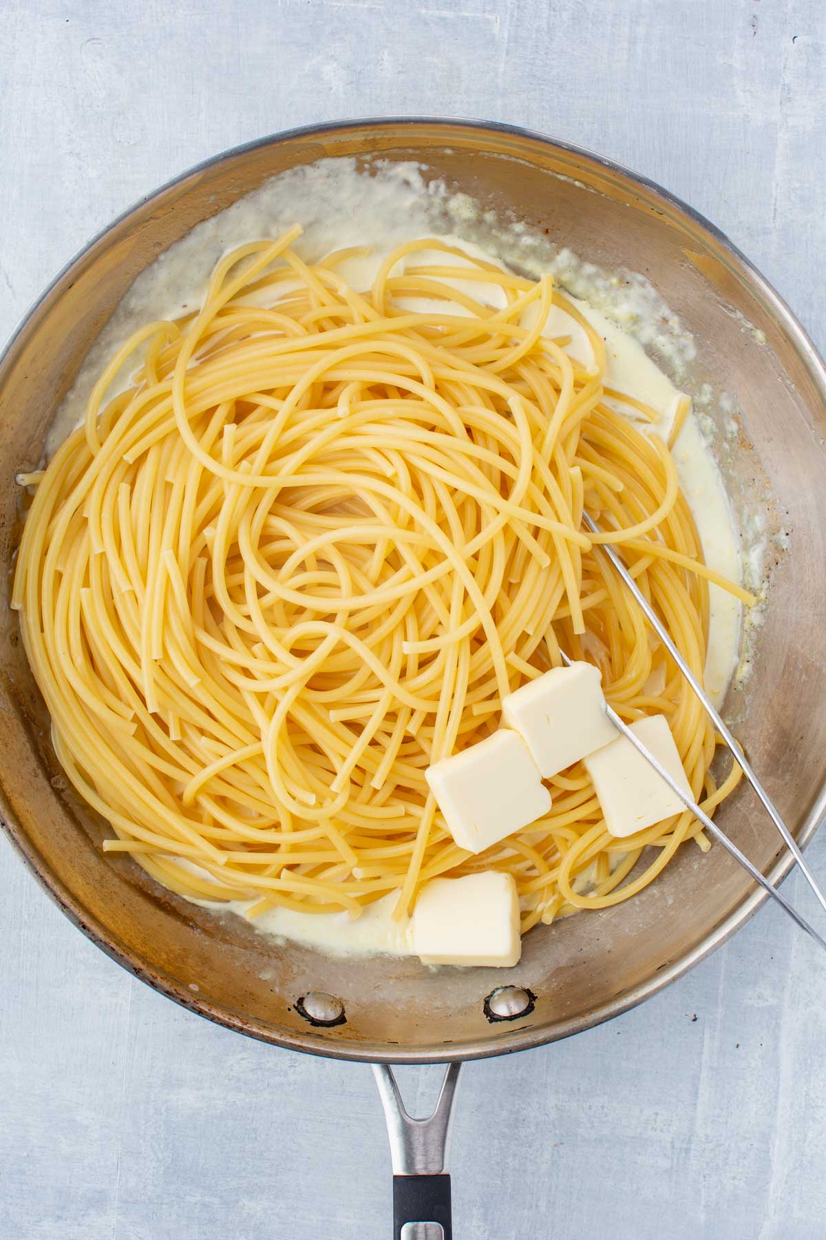 Cooked spaghetti and cubes of butter added to a skillet of lemon cream sauce, ready to be tossed together for pasta al limone.