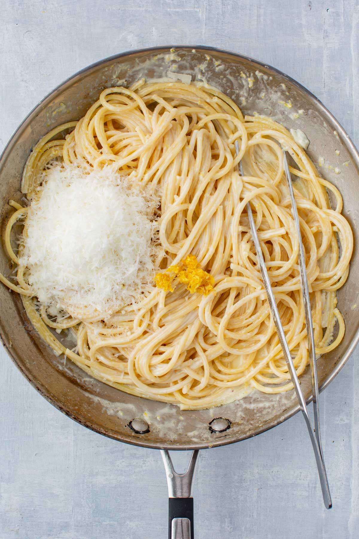 Freshly grated Parmesan cheese and lemon zest added to creamy spaghetti in a skillet-finishing touches for pasta al limone.