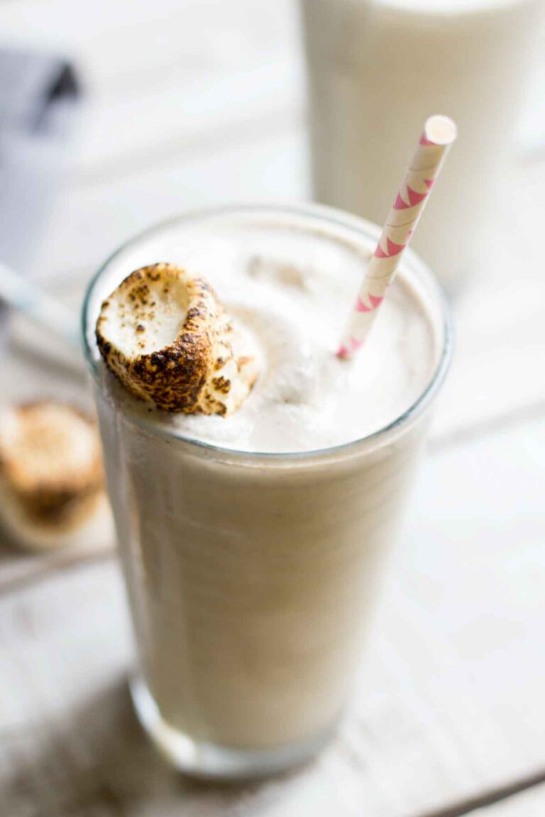 Side view of a toasted marshmallow milkshake in a tall clear glass with a pink-striped straw and a perfectly browned marshmallow garnish.