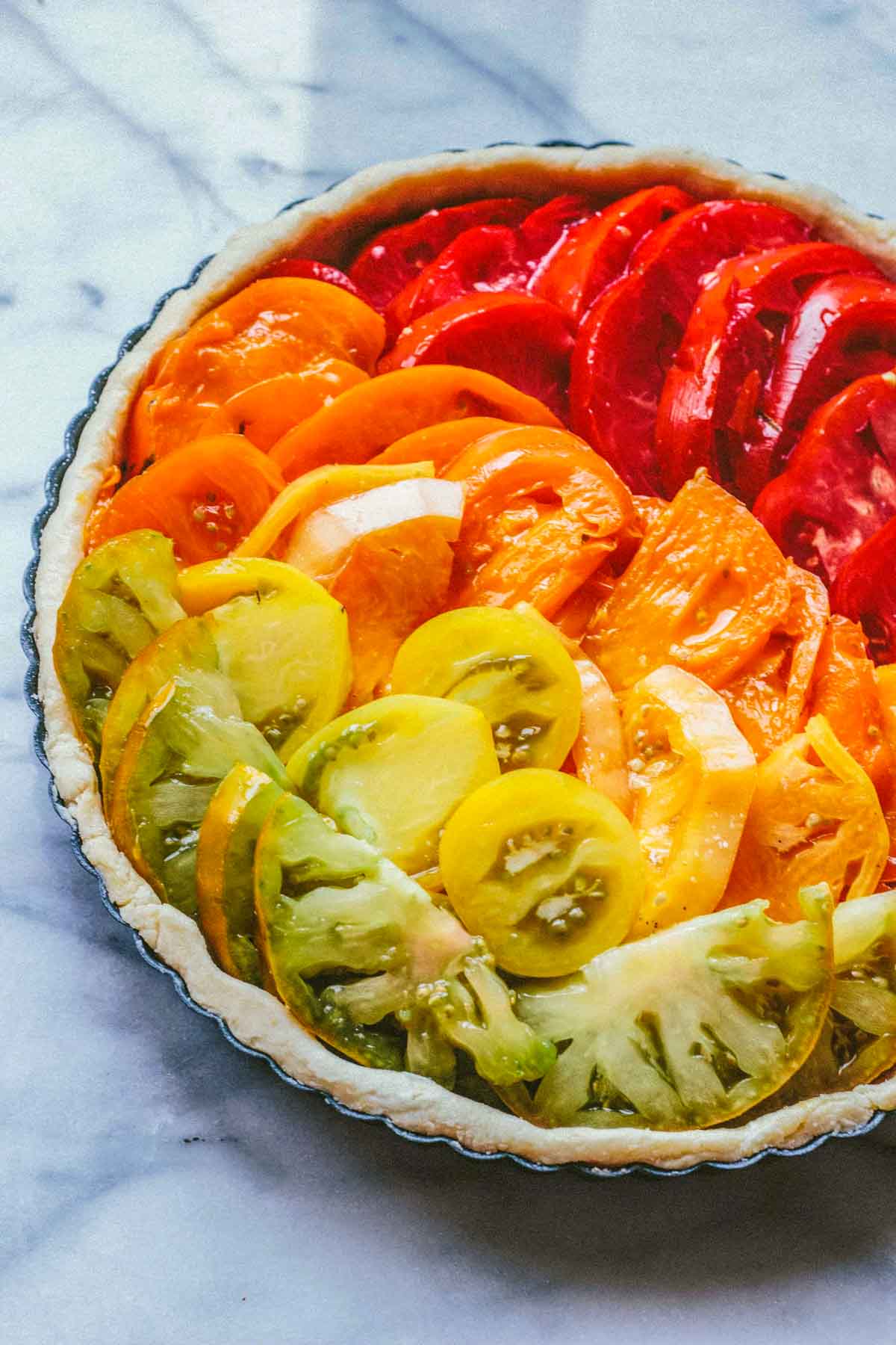 Unbaked tomato tart arranged with colorful heirloom tomato slices in a rainbow gradient over a flaky pastry crust, ready for the oven.